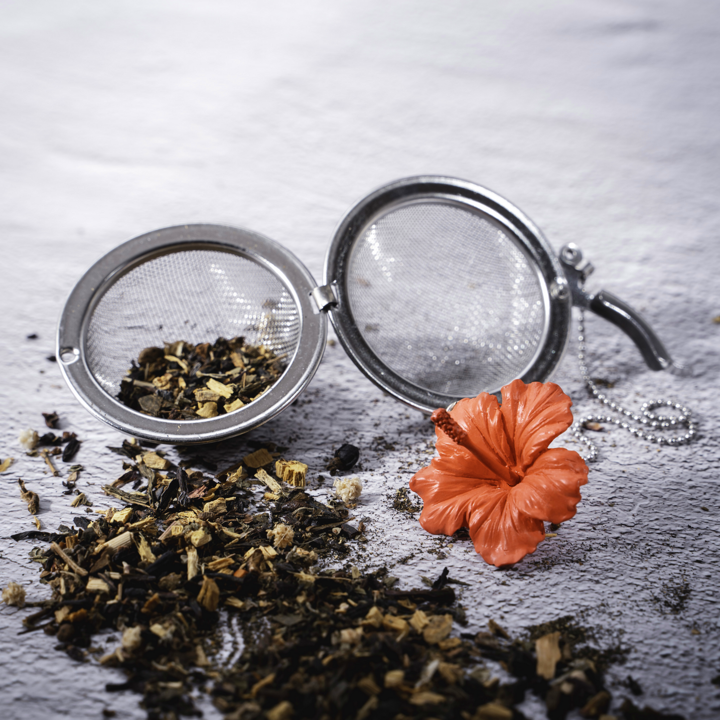 01Living Stainless steel Loose Leaf Tea Ball Infuser with Hibiscus Flower Red Charm, filled with loose-leaf tea spilling out onto bench, allowing tea leaves to be seen.