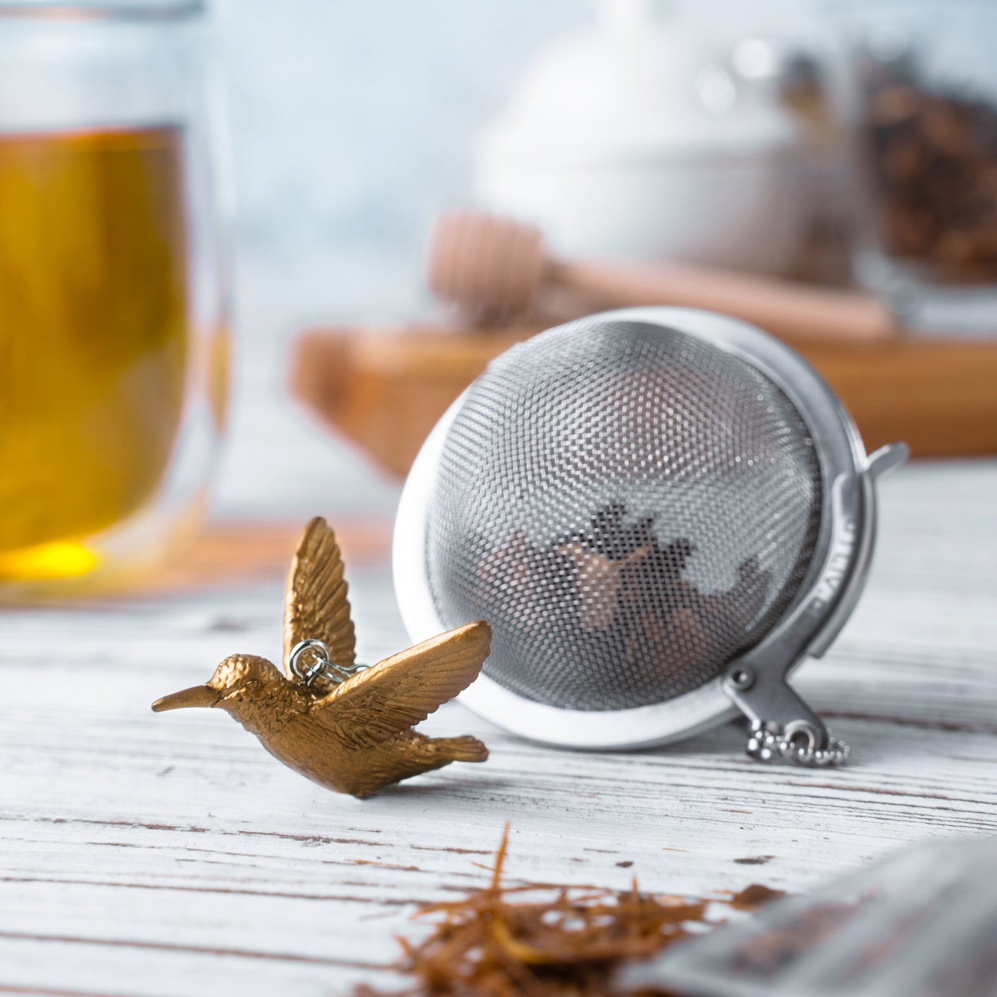 ChiChi Loose Leaf Tea Ball Infuser steeping loose-leaf tea in a cup, with its decorative Hummingbird charm in Gold finish and chain adding a playful touch to the tea ritual.