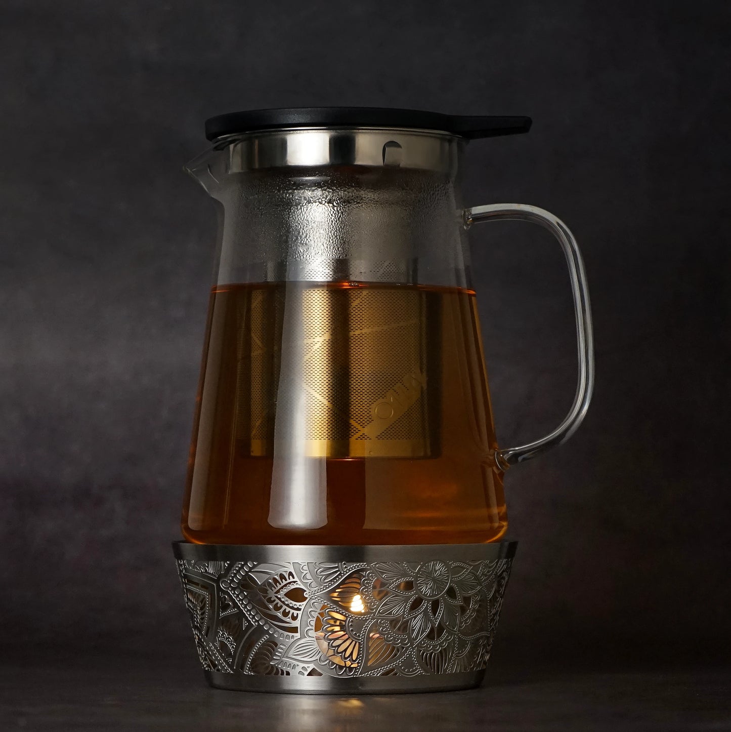 Silver Mandala Tea Warmer holding a 1L glass teapot over a lit tealight candle, creating a warm and relaxing tea setting.