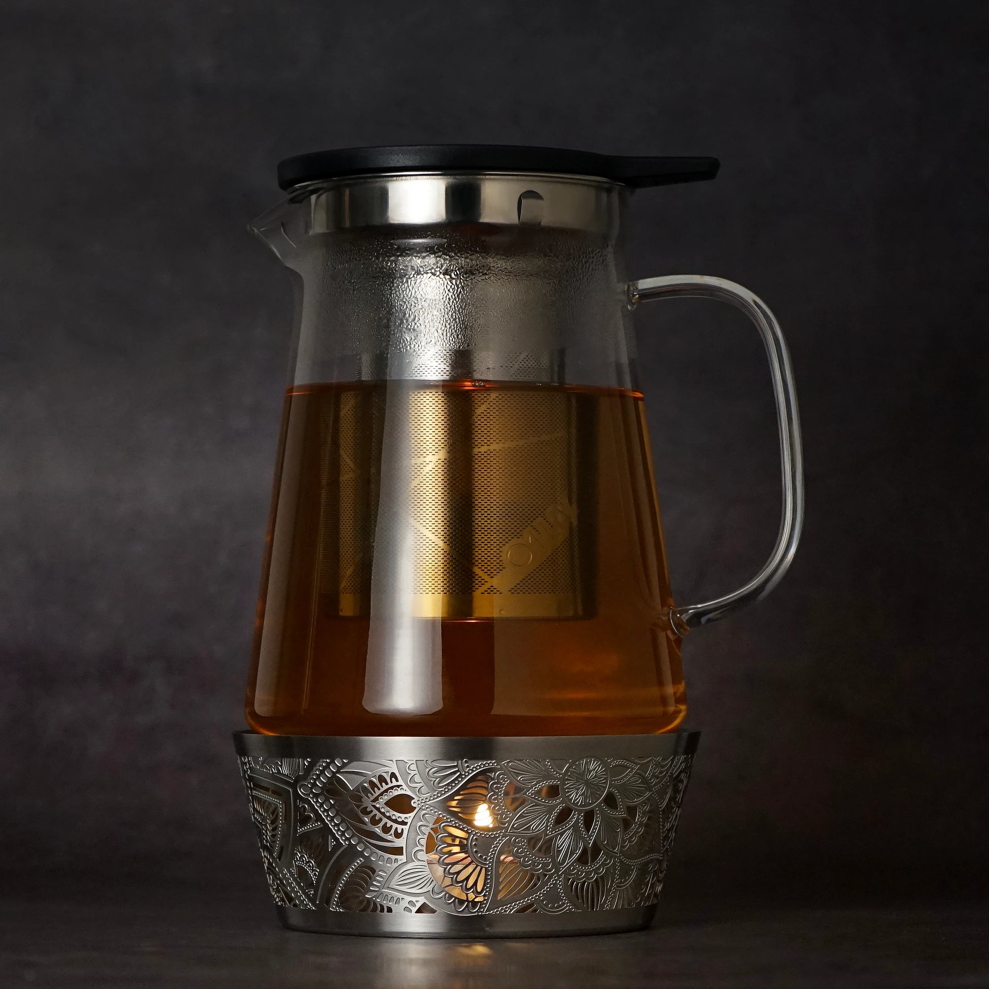 Silver Mandala Tea Warmer holding a 1L glass teapot over a lit tealight candle, creating a warm and relaxing tea setting.