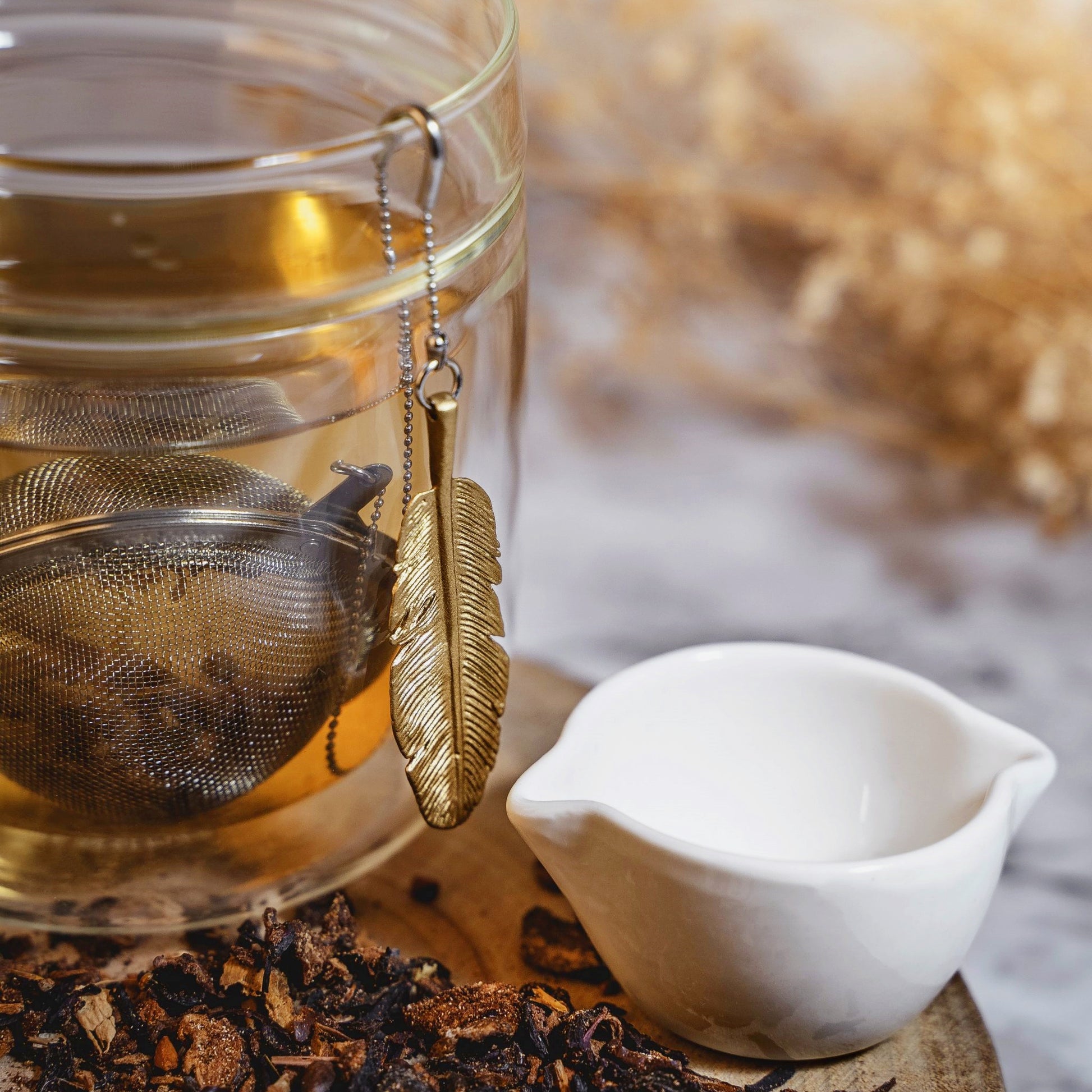 Loose Leaf Tea Ball Infuser steeping loose-leaf tea in a cup, with its decorative gold feather charm and patent u-hook chain adding a playful touch to the tea ritual.
