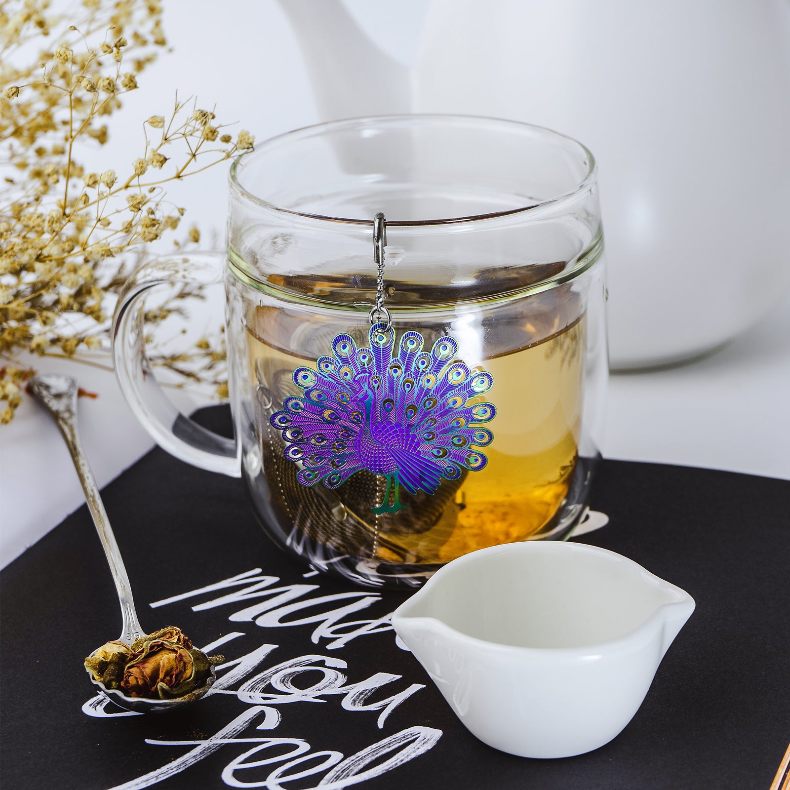 Stainless steel Loose Leaf Tea Ball Infuser with a multicoloured Peacock charm filled with loose-leaf tea and suspended in a cup, allowing tea leaves to steep while keeping sediment contained.