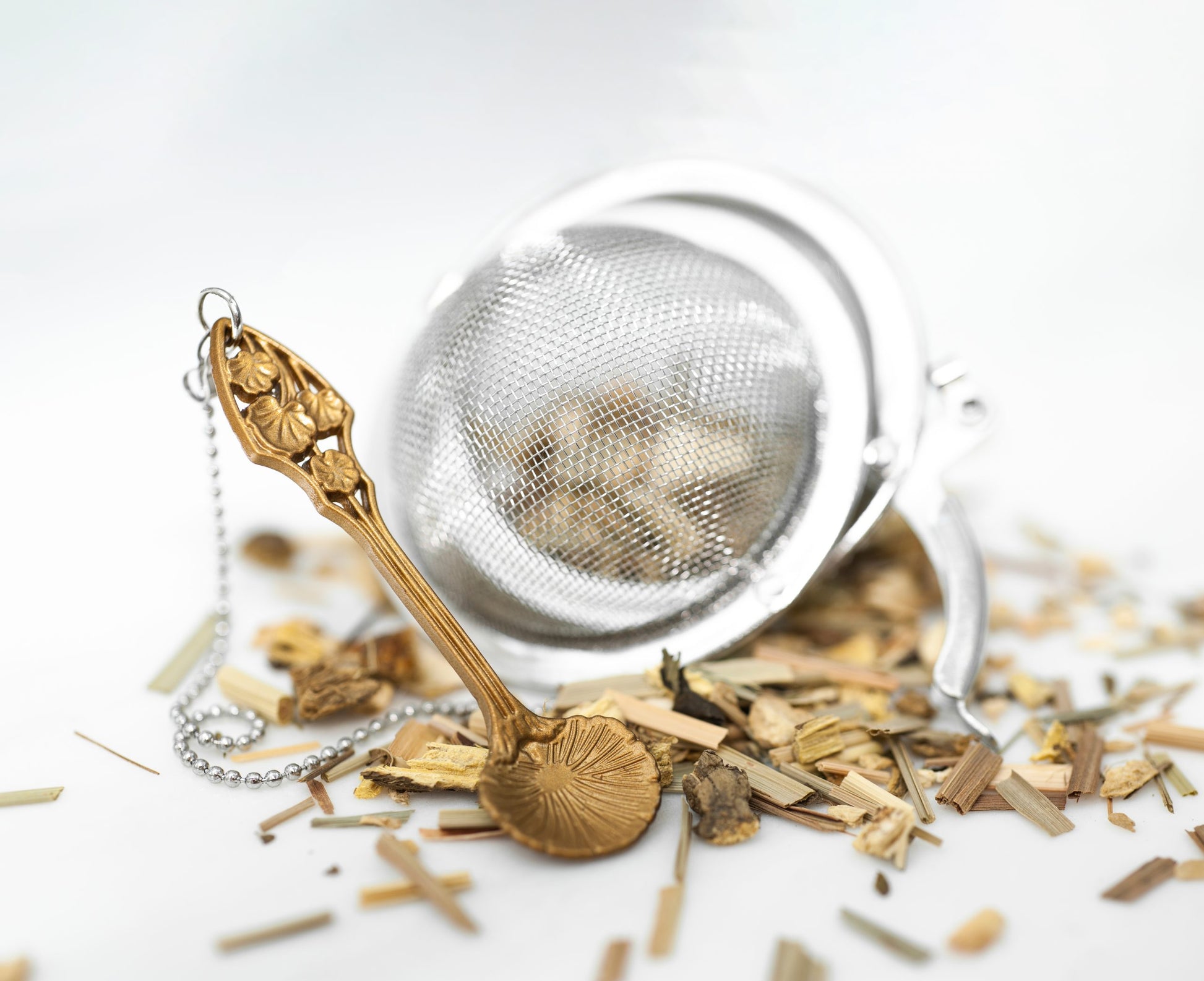 Stainless steel Loose Leaf Tea Ball Infuser with a gold Lobed Spoon charm, open with loose-leaf tea spilling out.