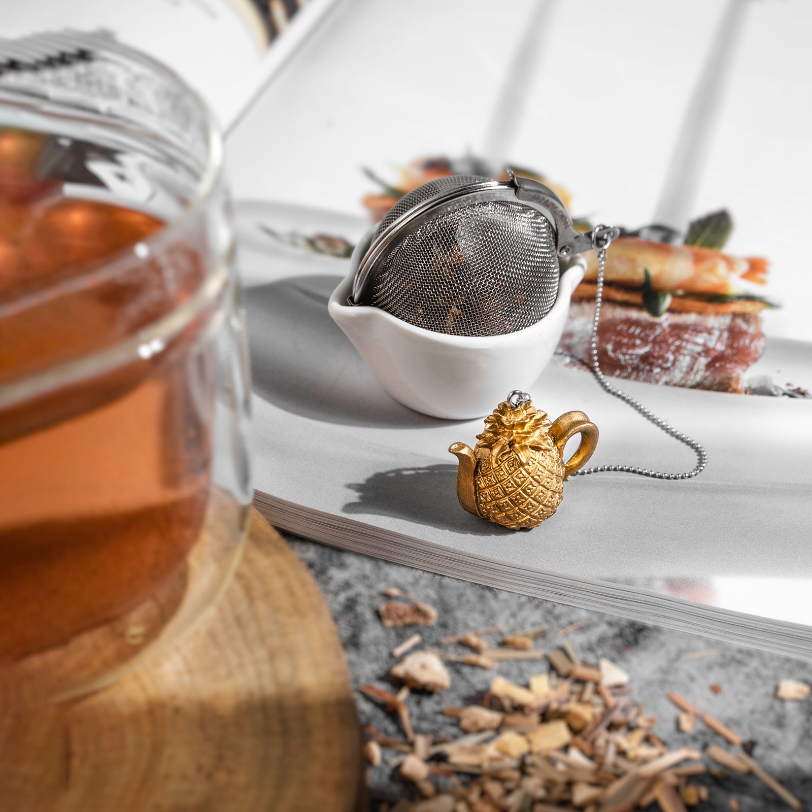Stainless steel Loose Leaf Tea Ball Infuser filled with loose-leaf tea sitting alongside a cup and magazine.