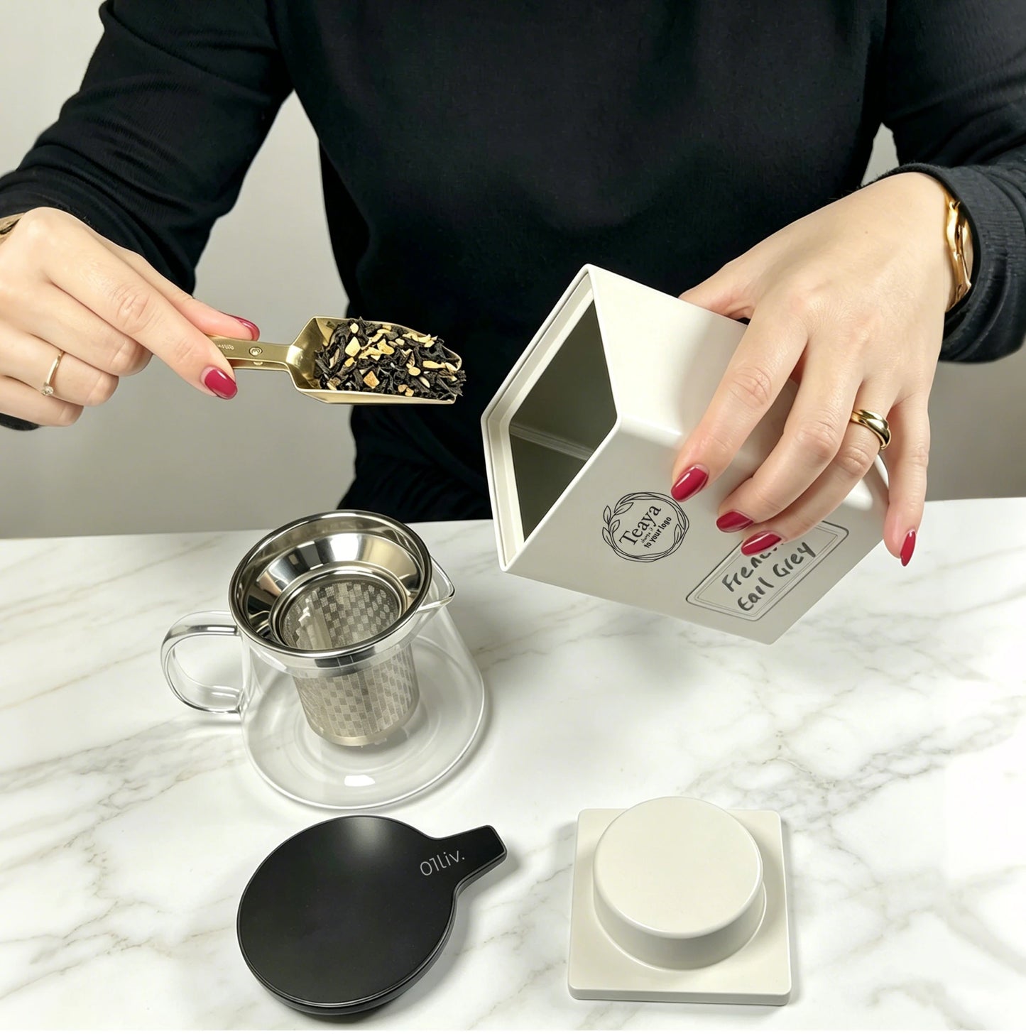 A person in a black top demonstrates scooping loose leaf tea from a Matte white Square Tea & Coffee Canister displayed on a kitchen bench alongside premium teaware and brewing accessories.